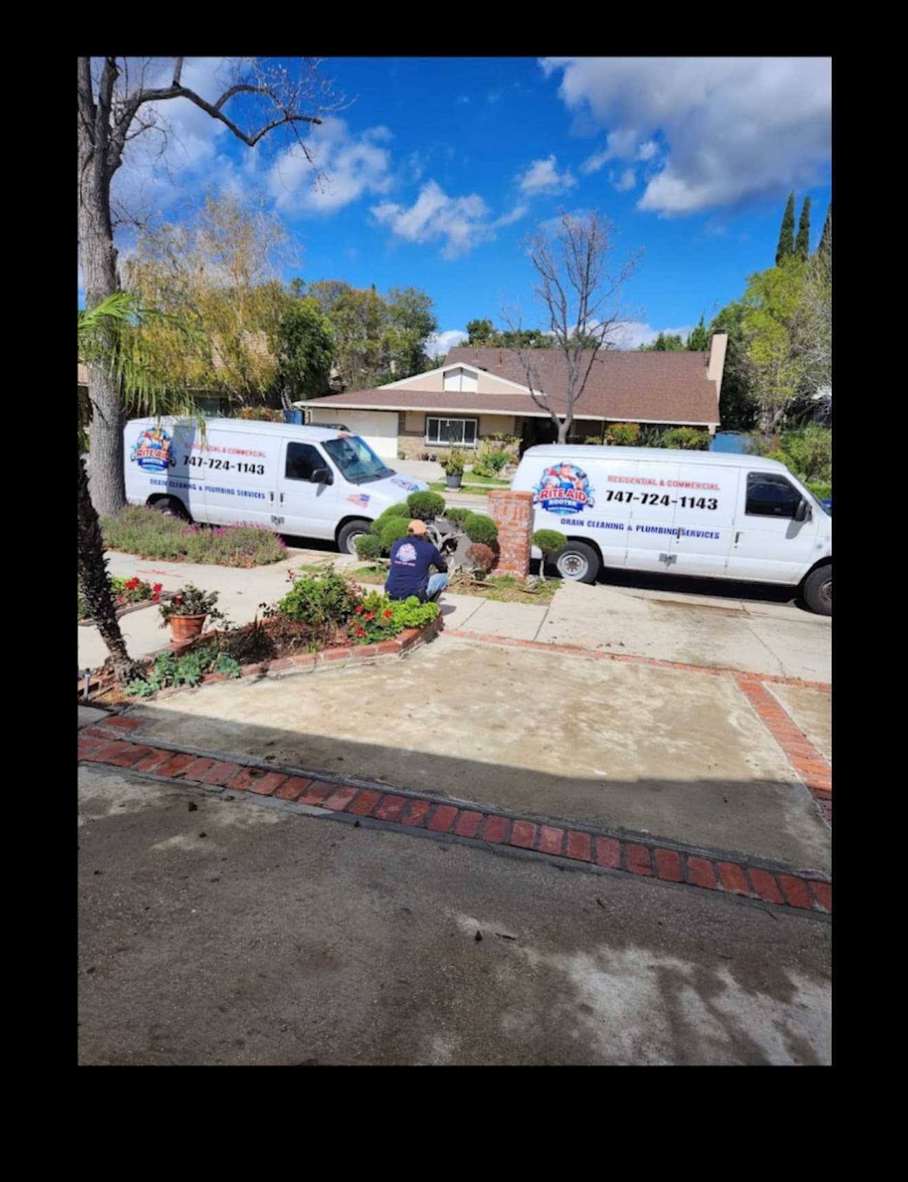Two Rite Aid Rooter plumbing vans parked at a suburban home with a technician working.