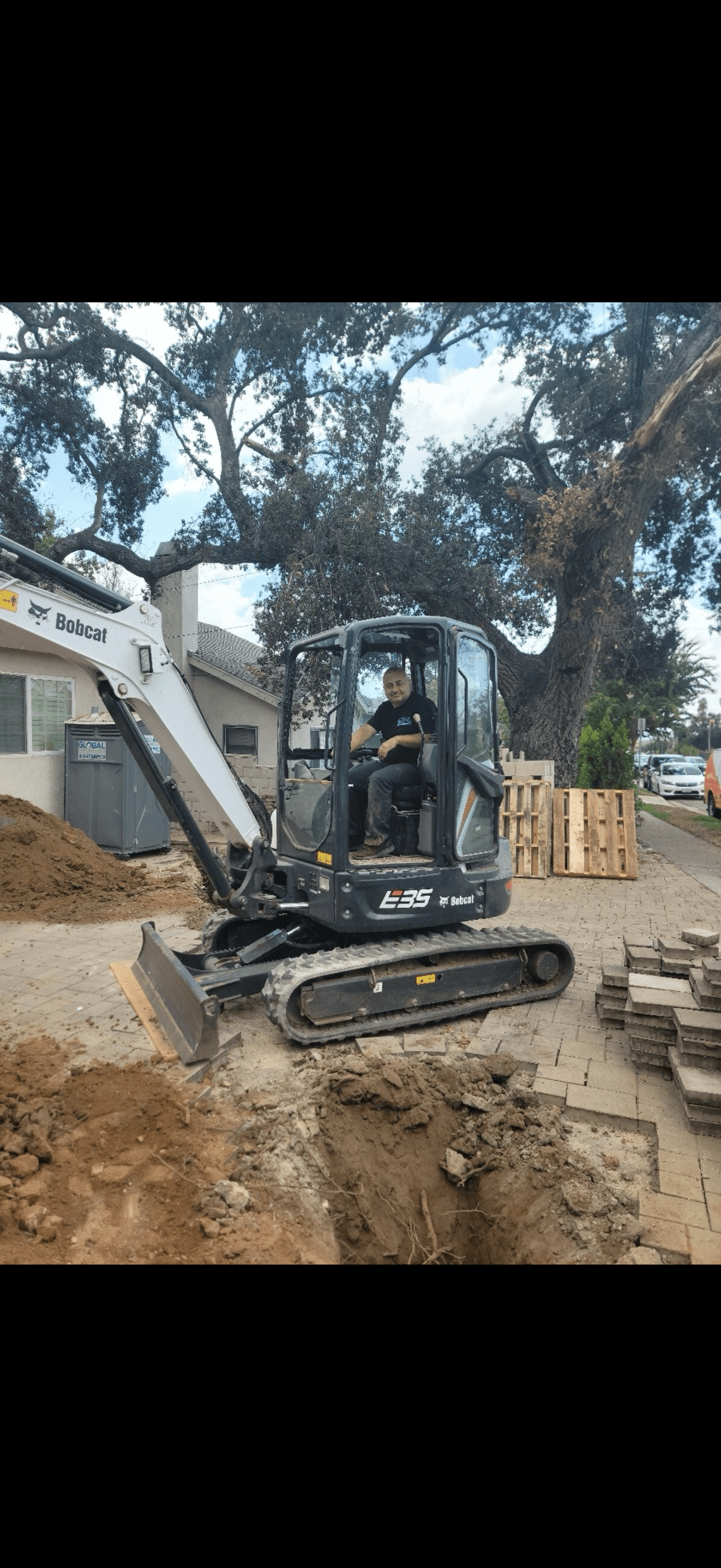 Man operating a Bobcat E35 excavator at a residential site with dirt and pavers.
