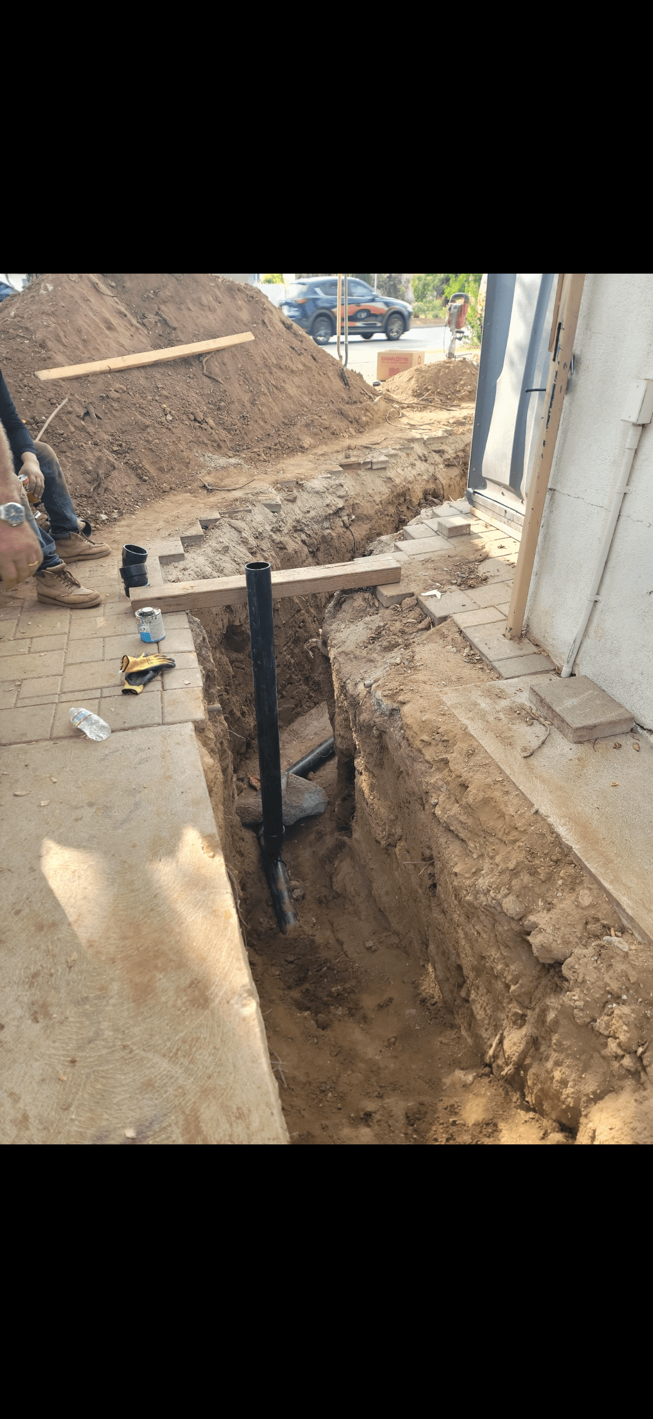 Vertical black pipe installed in a deep dirt trench at a residential construction site.